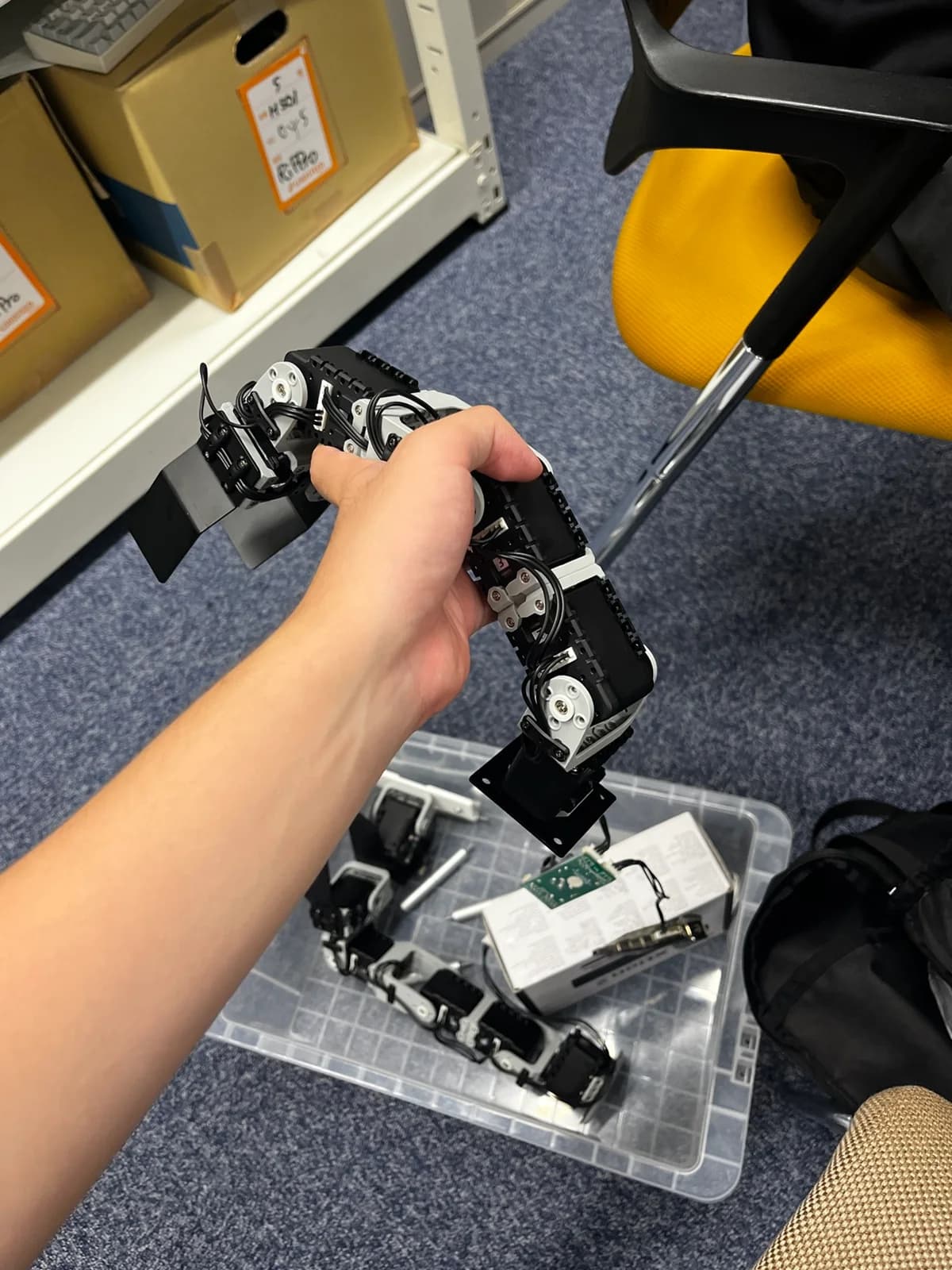 A robotic arm assembly being held above a container of hardware components during an early development session.